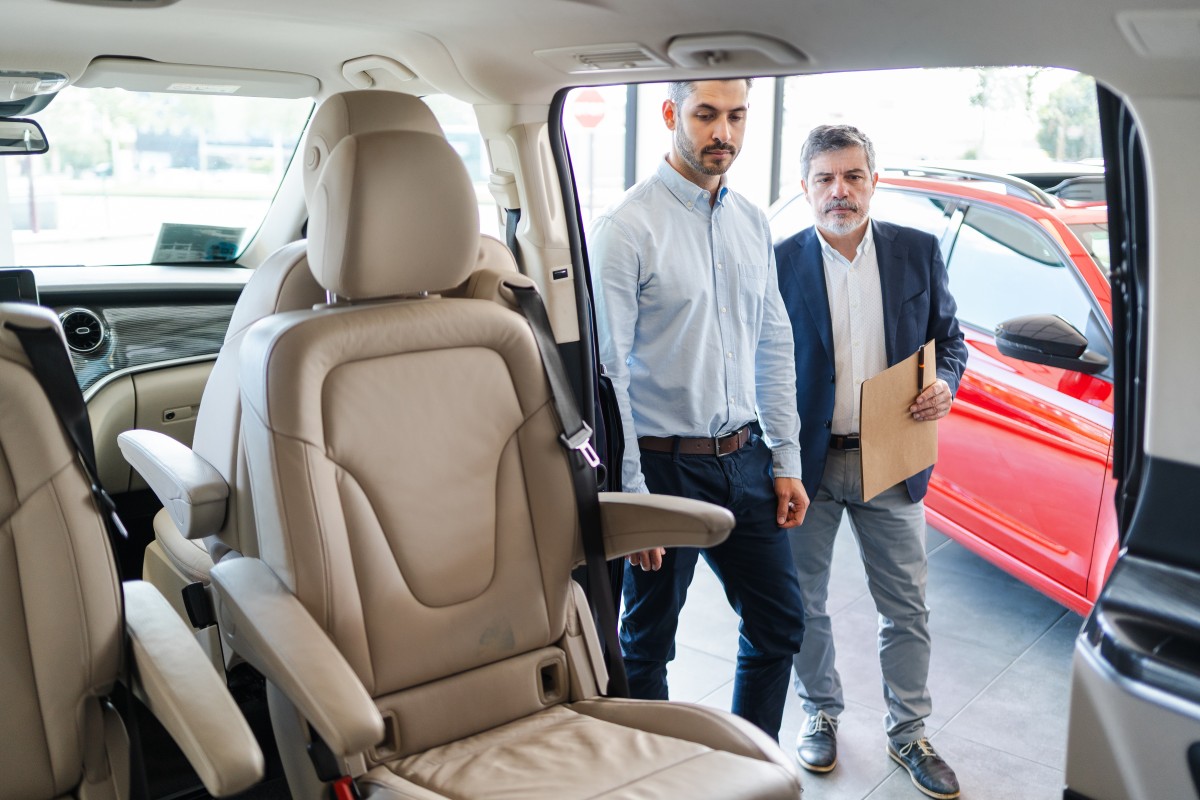 Comprador a receber chaves de um carro usado numa concessionária, com documentação sobre a mesa