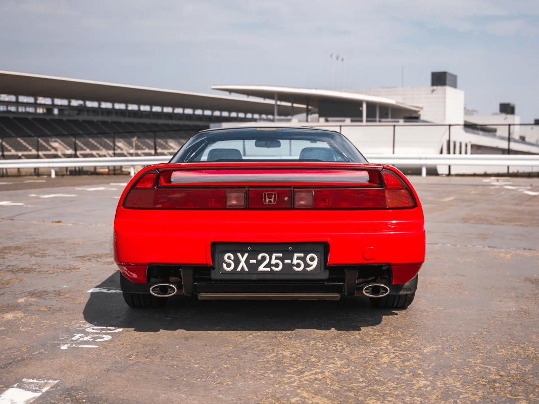 Honda NSX de primeira geração em tom amarelo canário ou vermelho, fotografado de perfil em ambiente de circuito ou estrada aberta