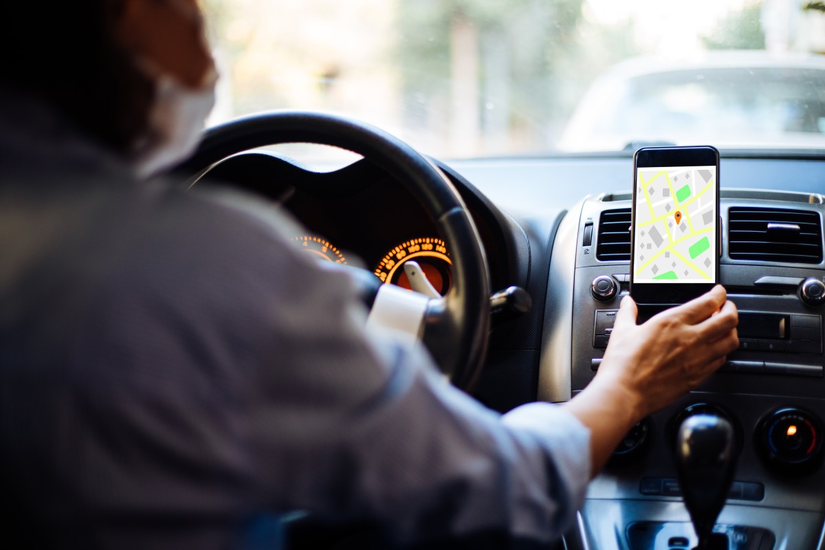 Condutor a consultar o telemóvel com app de navegação no suporte do painel de instrumentos, em contexto de trânsito urbano