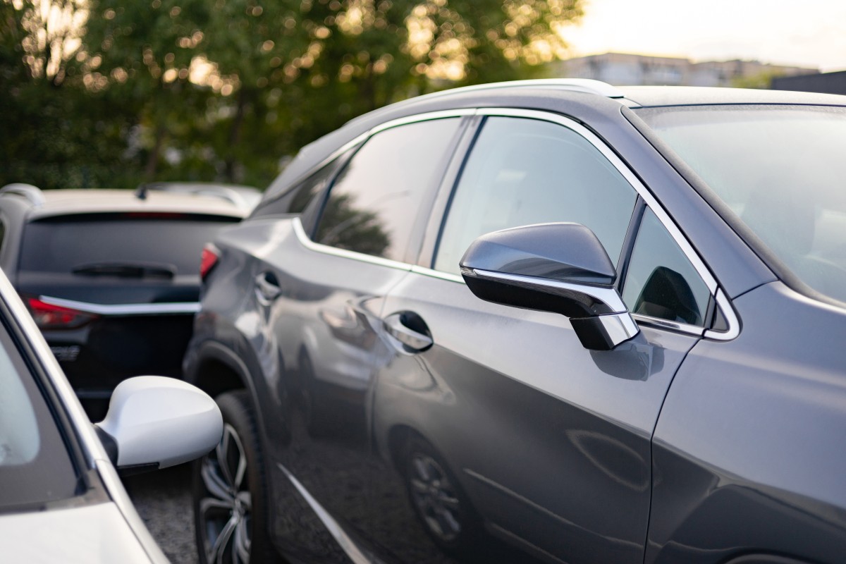comprador a inspeccionar o exterior de um carro usado num parque de estacionamento durante o dia